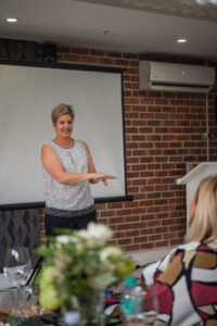 woman in a dotted white shirt and black pants speaking at the Accelerate Action: A Creative Brunch for Women in Business Leadership function