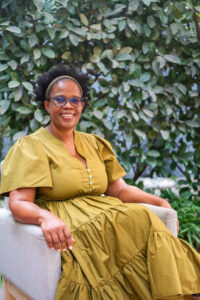 woman in a green dress sitting outside and smiling at the camera at the Accelerate Action: A Creative Brunch for Women in Business Leadership function