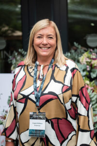 woman in a multicoloured outfit smiling at the camera in front of the "Bloom Bar" sign at the Accelerate Action: A Creative Brunch for Women in Business Leadership function