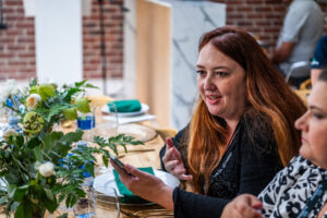 woman at a long dining table conversing with other people at her table