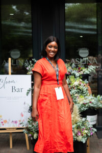 women in orange dress smiling. Next to her is a sign saying "Bloom Bar"