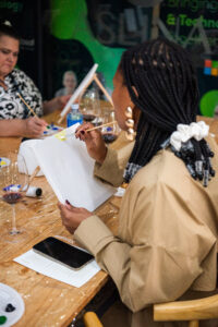 Women fat the Accelerate Action: A Creative Brunch for Women in Business Leadership function, painting on small canvasses and having wine -2