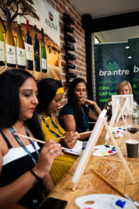 Women fat the Accelerate Action: A Creative Brunch for Women in Business Leadership function, painting on small canvasses and having wine