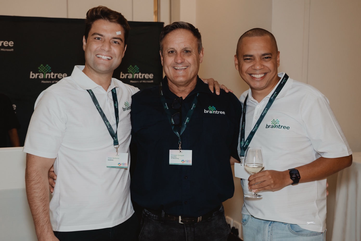 Three guests smiling together in front of the branded backdrop