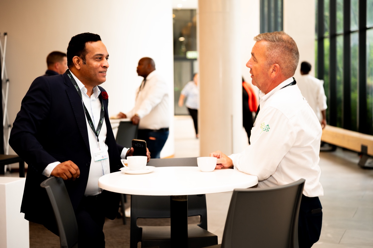 Two guests chatting over coffee at a table in a bright networking area.