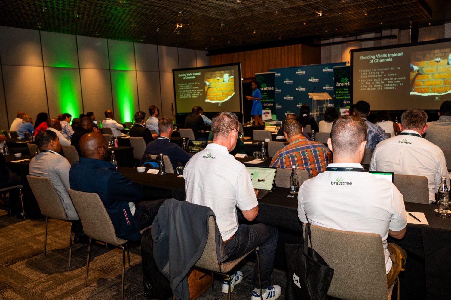 Attendees seated at tables during a session with green stage lighting