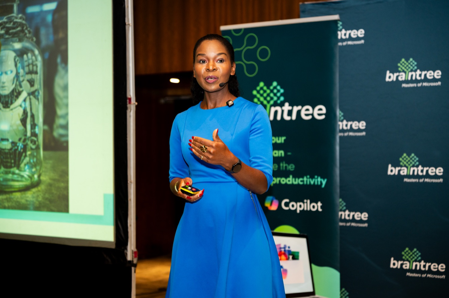 A speaker in a blue dress presenting beside a Braintree banner