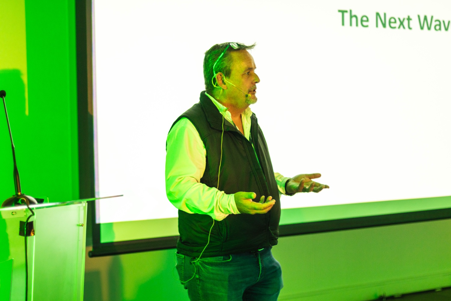 A speaker addressing the room in front of The Next Wave slide