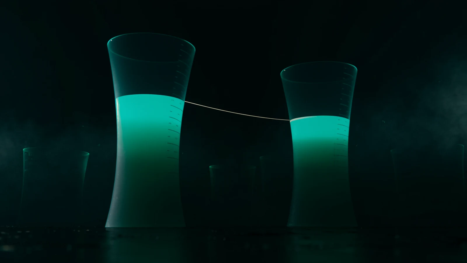 Two tall translucent vessels standing side by side in darkness, filled to visibly different levels, with a thin taut filament of light stretched between them.